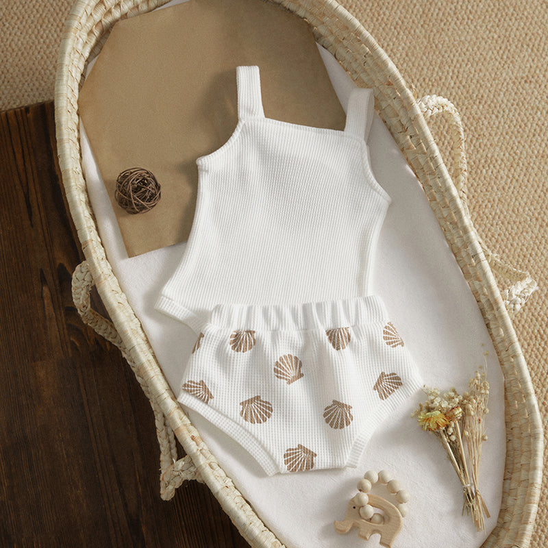 White sleeveless top and shell-patterned shorts on a white blanket with decorative elements.