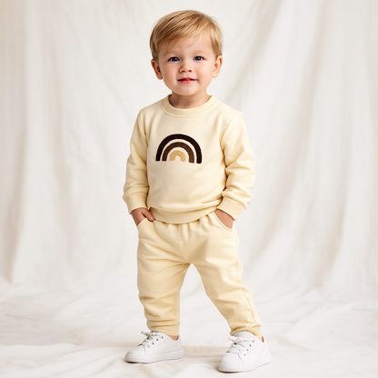 Child wearing a beige sweatshirt with a rainbow design and matching pants on a white background